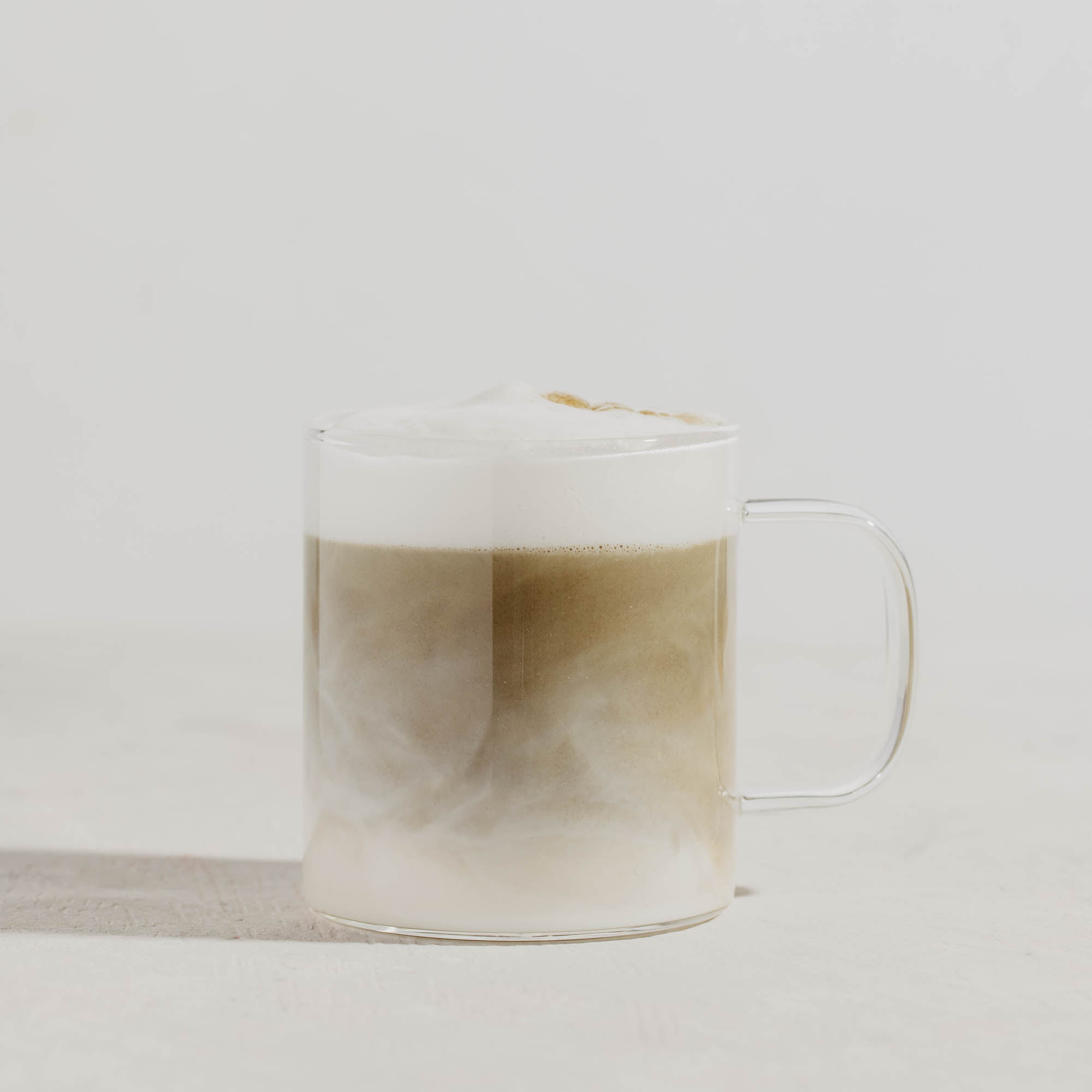 Glastasse mit Houjicha Latte und Schaumkrone auf weiß